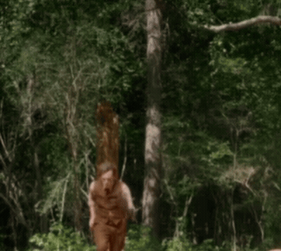 A Man In A Brown Vest And Pants Is Walking Through A Forest GIF