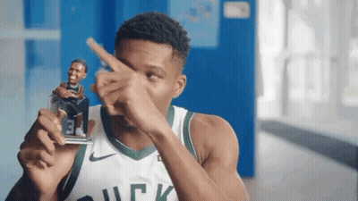 A Man In A Bucks Jersey Is Holding A Figurine Of A Basketball Player And Pointing At It . GIF