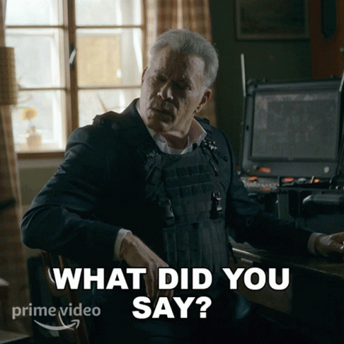 A Man In A Bullet Proof Vest Is Sitting At A Desk And Says What Did You Say GIF