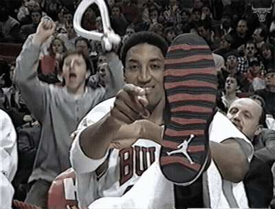 A Man In A Bulls Jersey Holds Up His Shoe In Front Of A Crowd GIF
