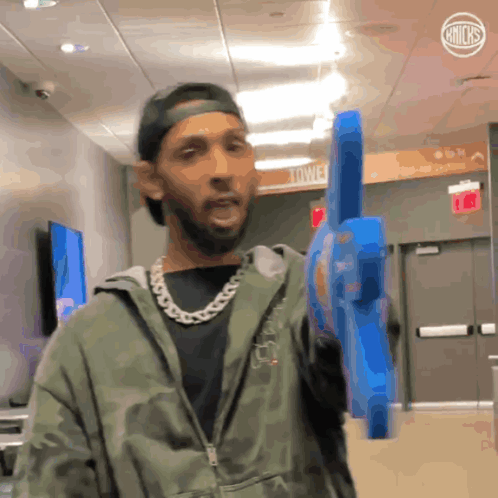 A Man In A Camo Jacket Holds A Blue Toy Gun In A Hallway GIF
