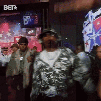 A Man In A Camo Jacket Is Dancing In Front Of A Crowd Of People . GIF