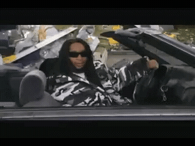 A Man In A Camouflage Jacket Is Sitting In A Car With His Feet Up . GIF