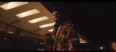 A Man In A Camouflage Jacket Is Standing In A Dark Room With A Ceiling Light . GIF