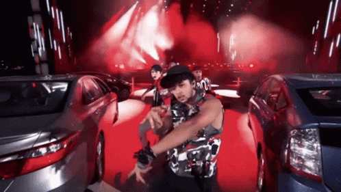 A Man In A Camouflage Shirt Is Dancing In Front Of A Crowd Of Cars GIF