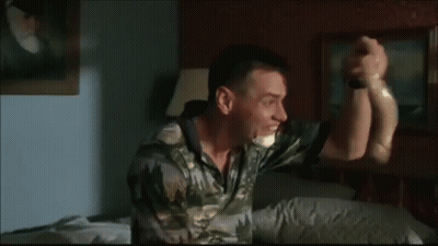 A Man In A Camouflage Shirt Is Sitting On A Bed With His Hand On His Head . GIF