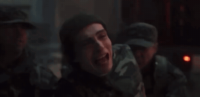 A Man In A Camouflage Uniform Is Laughing In A Dark Room With Other Men . GIF