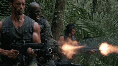 A Man In A Camouflage Vest Is Holding A Gun With The Letter O On The Barrel GIF