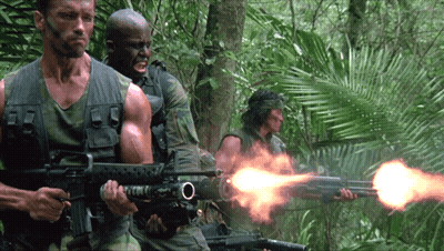 A Man In A Camouflage Vest Is Holding A Rifle With The Letter O On The Barrel GIF