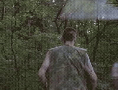 A Man In A Camouflage Vest Is Running Through The Woods With A Smoke Bomb . GIF