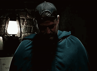 A Man In A Cape Covering His Face With His Hands In A Dark Room GIF