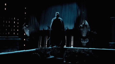 A Man In A Cape Is Standing In Front Of A Building GIF