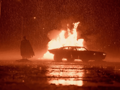 A Man In A Cape Is Standing Next To A Burning Car GIF