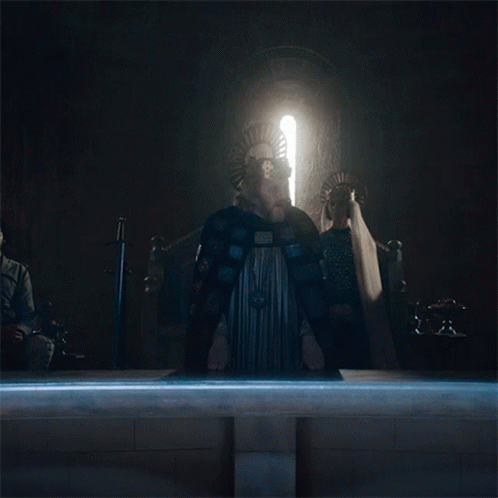 A Man In A Cape Stands In Front Of A Window With A Light Shining Through It GIF