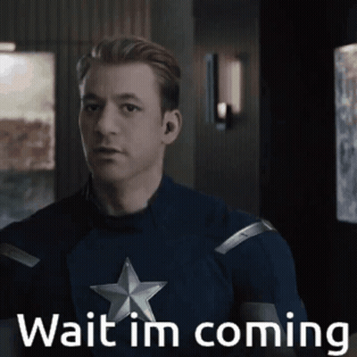 A Man In A Captain America Costume Is Standing In A Room And Says Wait I 'M Coming . GIF