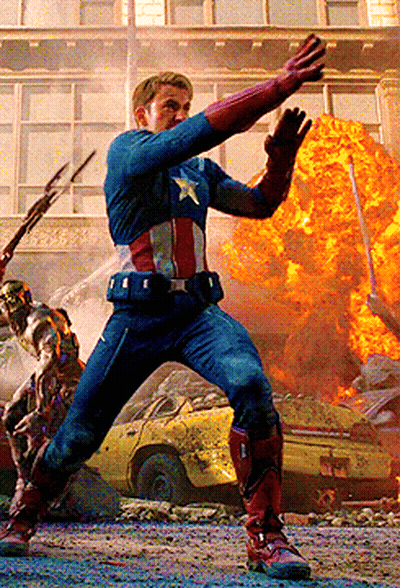 A Man In A Captain America Costume Is Standing In Front Of A Huge Explosion GIF