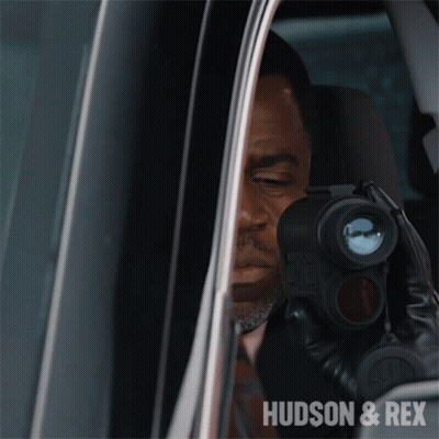 A Man In A Car Looking Through A Binoculars With The Words Hudson & Rex On The Bottom Right GIF