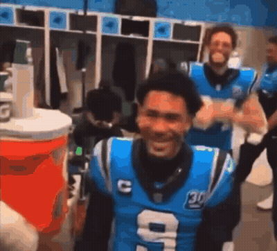 A Man In A Carolina Panthers Jersey Is Standing In A Locker Room . GIF