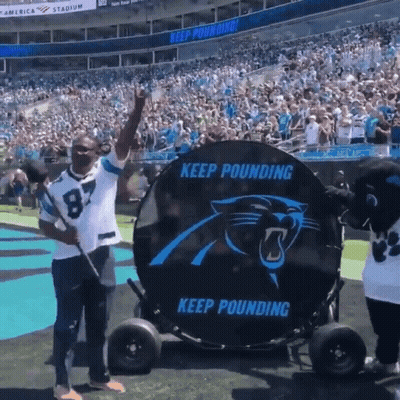 A Man In A Carolina Panthers Jersey Is Standing In Front Of A Large Keep Pounding Sign GIF