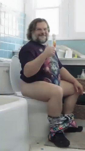 A Man In A Cat Shirt Is Sitting On A Toilet Holding A Drink GIF