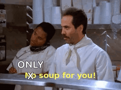 A Man In A Chef 'S Apron Is Standing In A Kitchen Talking On A Phone . GIF
