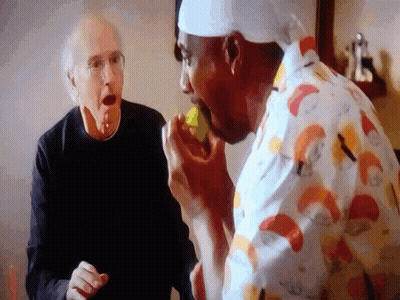 A Man In A Chef 'S Hat Is Eating A Lemon While Another Man Watches GIF