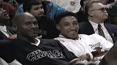 A Man In A Chicago Bulls Jersey Sits Next To Another Man GIF