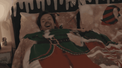 A Man In A Christmas Sweater Is Laying In A Bed GIF