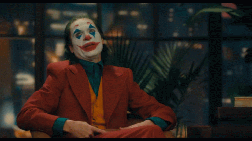 A Man In A Clown Costume Is Sitting In A Chair With His Mouth Open GIF
