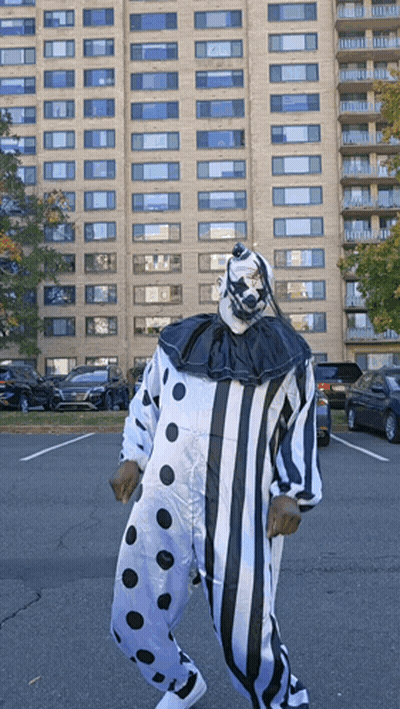 A Man In A Clown Costume Is Standing In A Parking Lot In Front Of A Tall Building GIF