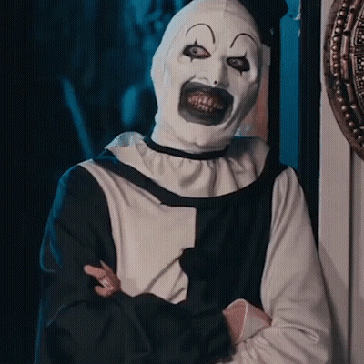 A Man In A Clown Costume Is Standing With His Arms Crossed . GIF