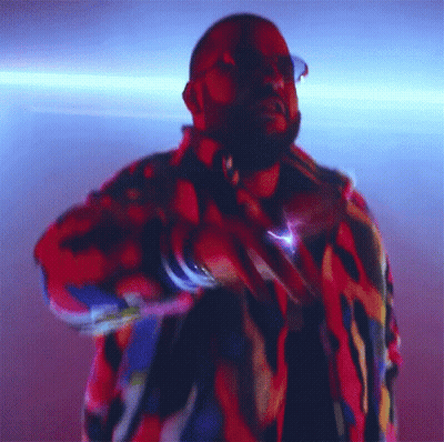 A Man In A Colorful Jacket Is Dancing In A Dark Room GIF