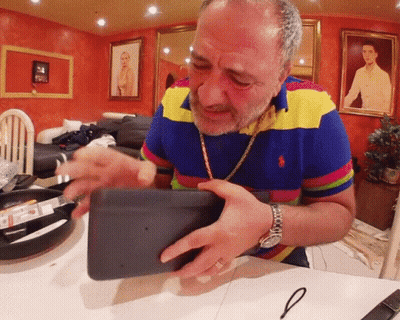 A Man In A Colorful Polo Shirt Is Holding A Black Object GIF