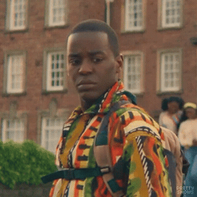 A Man In A Colorful Shirt And Backpack Is Standing In Front Of A Brick Building . GIF