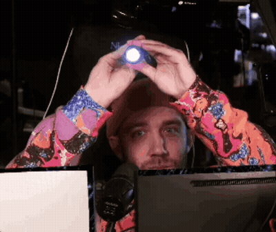 A Man In A Colorful Shirt Is Holding A Flashlight In Front Of His Head GIF