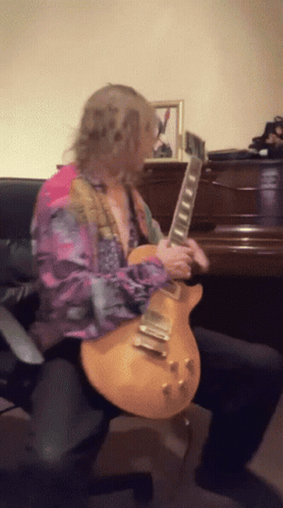 A Man In A Colorful Shirt Is Playing A Guitar In Front Of A Piano GIF