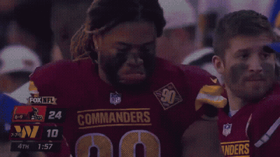 A Man In A Commanders Jersey Is Being Helped By Another Man GIF