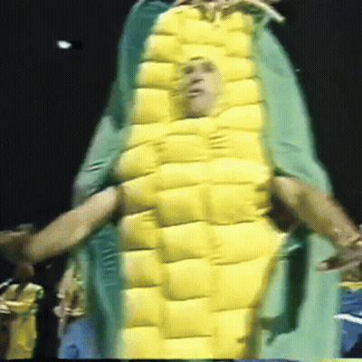A Man In A Corn On The Cob Costume Is Being Held By Another Man GIF