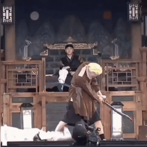 A Man In A Costume Is Holding A Sword While Another Man Watches GIF