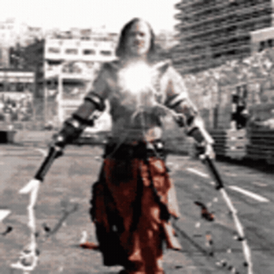 A Man In A Costume Is Holding Two Swords In Front Of A Building GIF