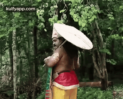 A Man In A Costume Is Standing In The Woods Holding An Umbrella . GIF