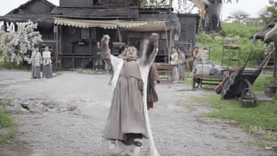 A Man In A Costume Is Standing On A Dirt Road Holding A Sword In His Hands . GIF
