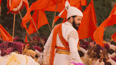 A Man In A Costume With A Beard Stands In Front Of A Crowd Of People Holding Orange Flags GIF