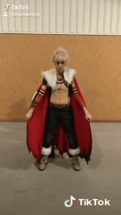 A Man In A Costume With A Red Cape Is Standing In Front Of A Wooden Wall . GIF