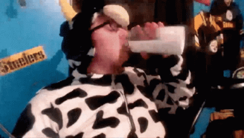 A Man In A Cow Costume Drinks From A Bottle GIF