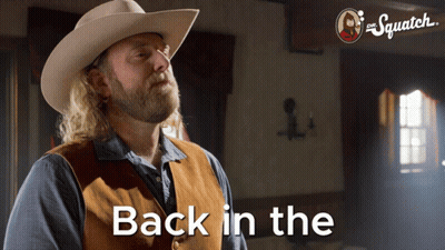 A Man In A Cowboy Hat And Vest Is Standing In Front Of A Sign That Says " Back In The " GIF