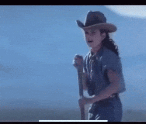 A Man In A Cowboy Hat Is Crawling On The Beach Near The Water . GIF