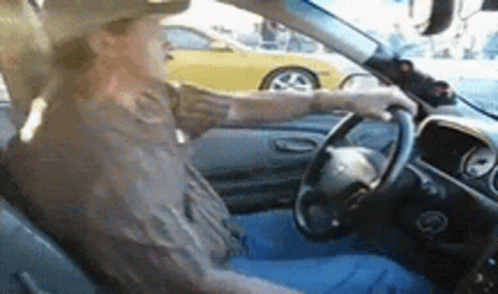 A Man In A Cowboy Hat Is Driving A Car With A Yellow Car In The Background . GIF