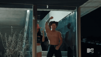 A Man In A Cowboy Hat Is Flexing His Muscles In Front Of A Tv Screen That Says Mtv GIF