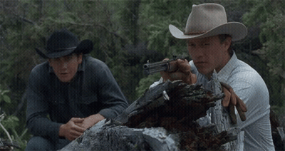 A Man In A Cowboy Hat Is Holding A Gun Next To Another Man GIF